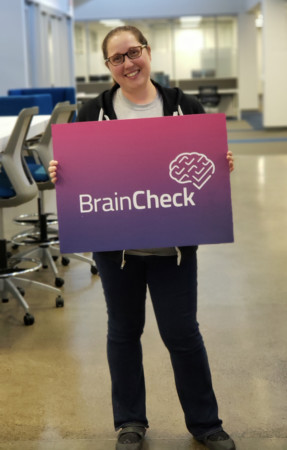 yael katz stands smiling and holding a brain check sign in front of her